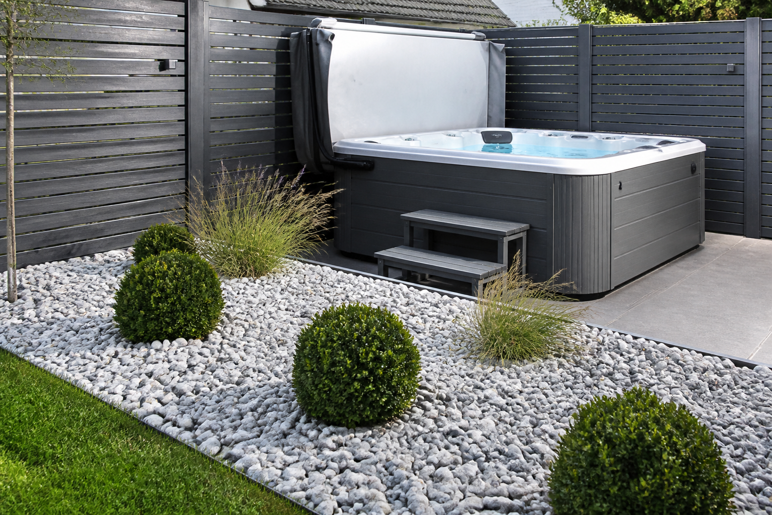 Contemporary grey hot tub with silver-grey granite pebble surround, slatted composite privacy screens, box ball shrubs and ornamental grasses in a modern UK garden